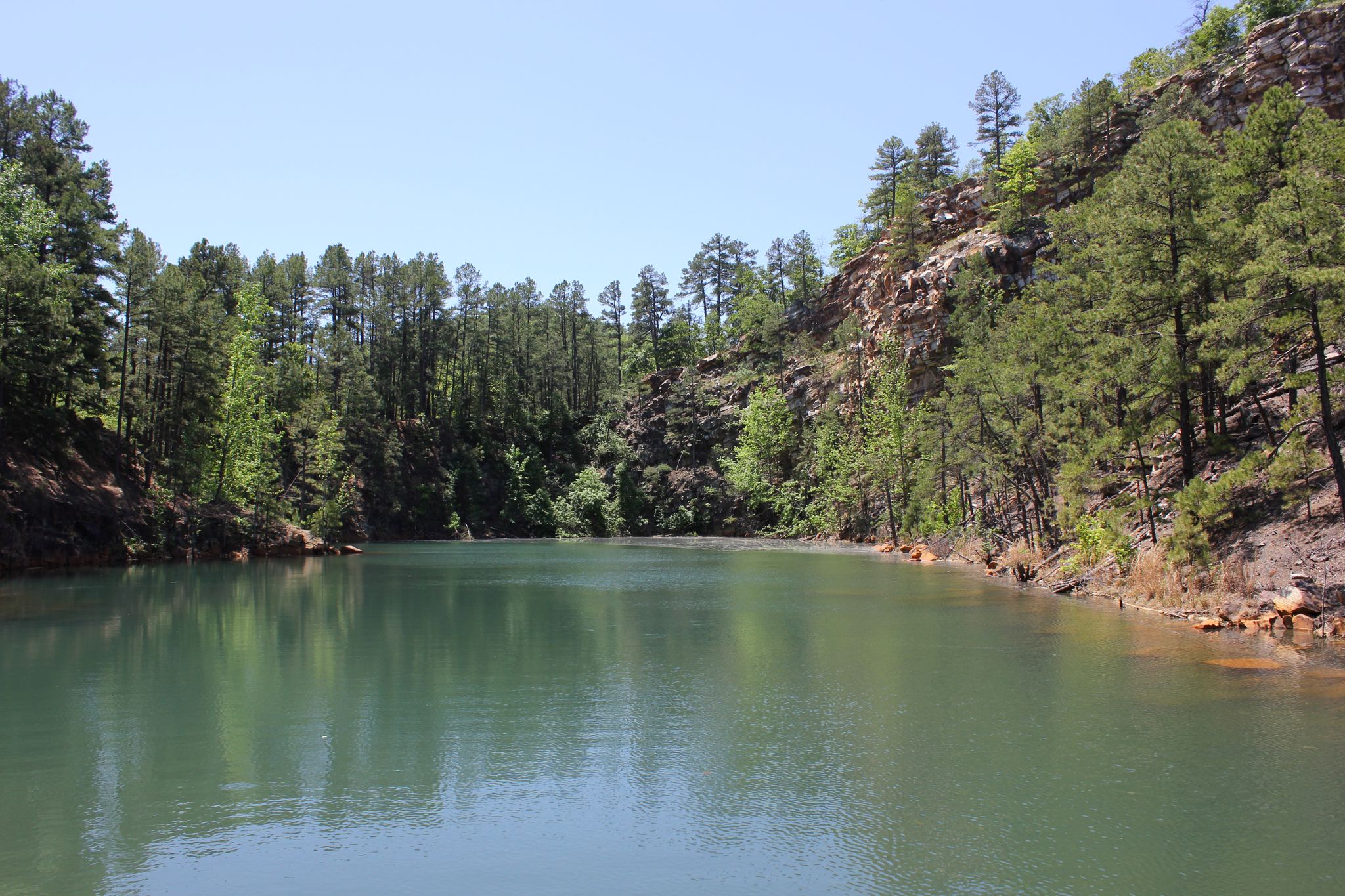 Calm green lake surrounded by steep, rocky, pine-covered hills on a sunny day. - Pinnacle Mountain State Park loop from Pinnacle Mountain