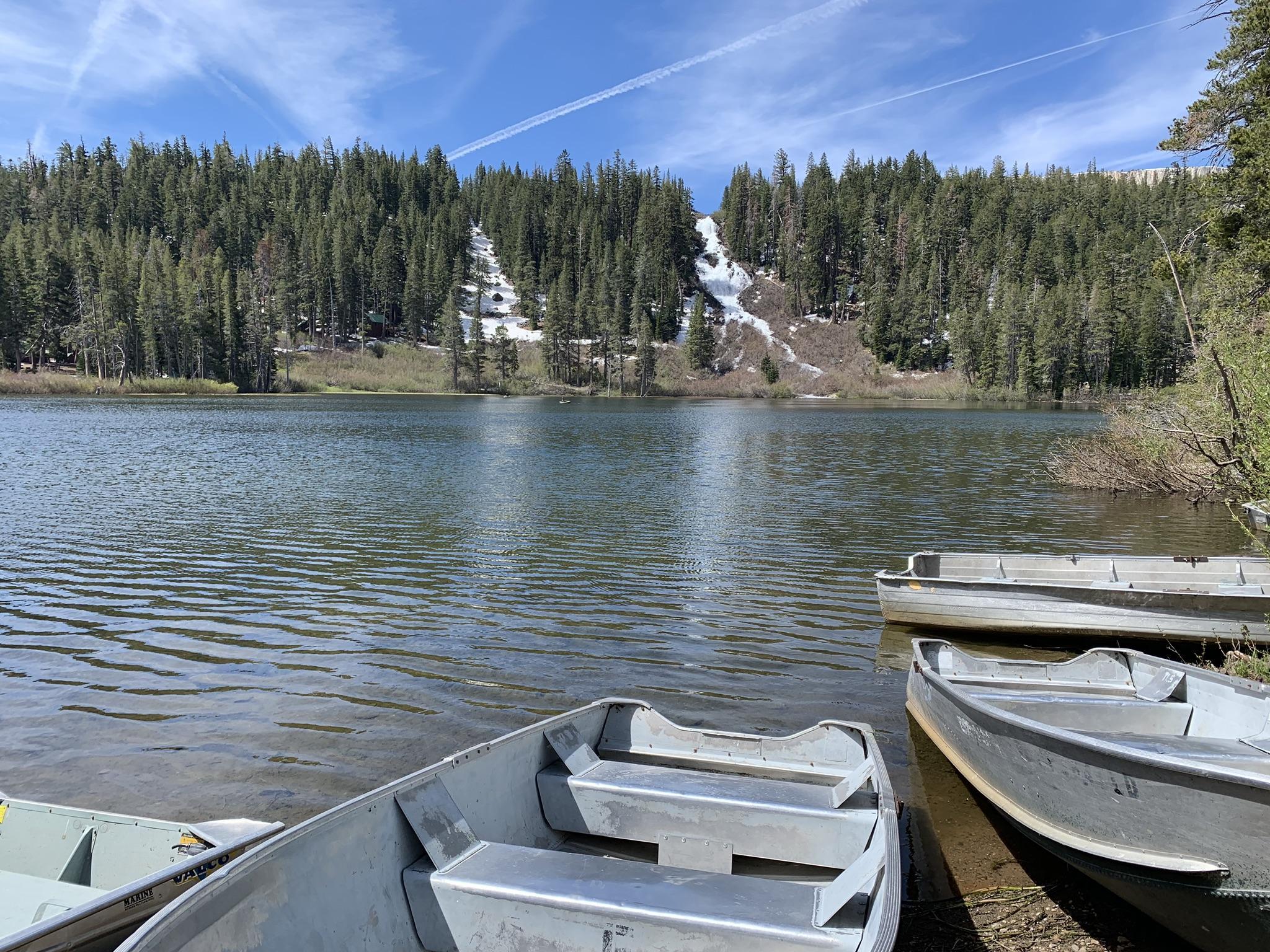 Empty rowboats on a lake shore, with a snowy forested hillside.