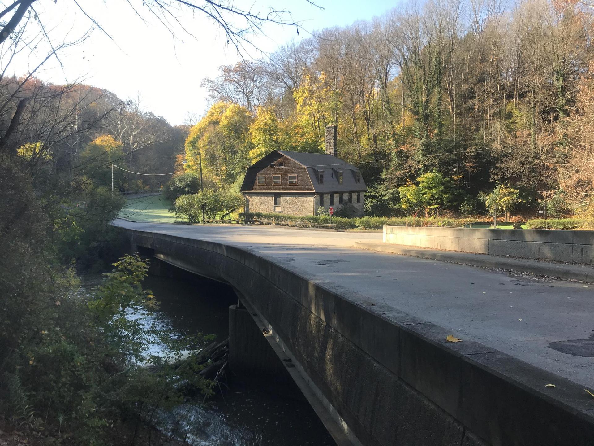 An old stone building next to a paved bridge, surrounded by autumn trees.