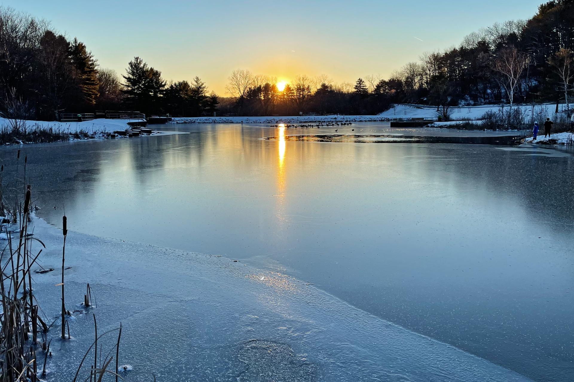 Golden sunset over a partially frozen lake surrounded by snowy banks.