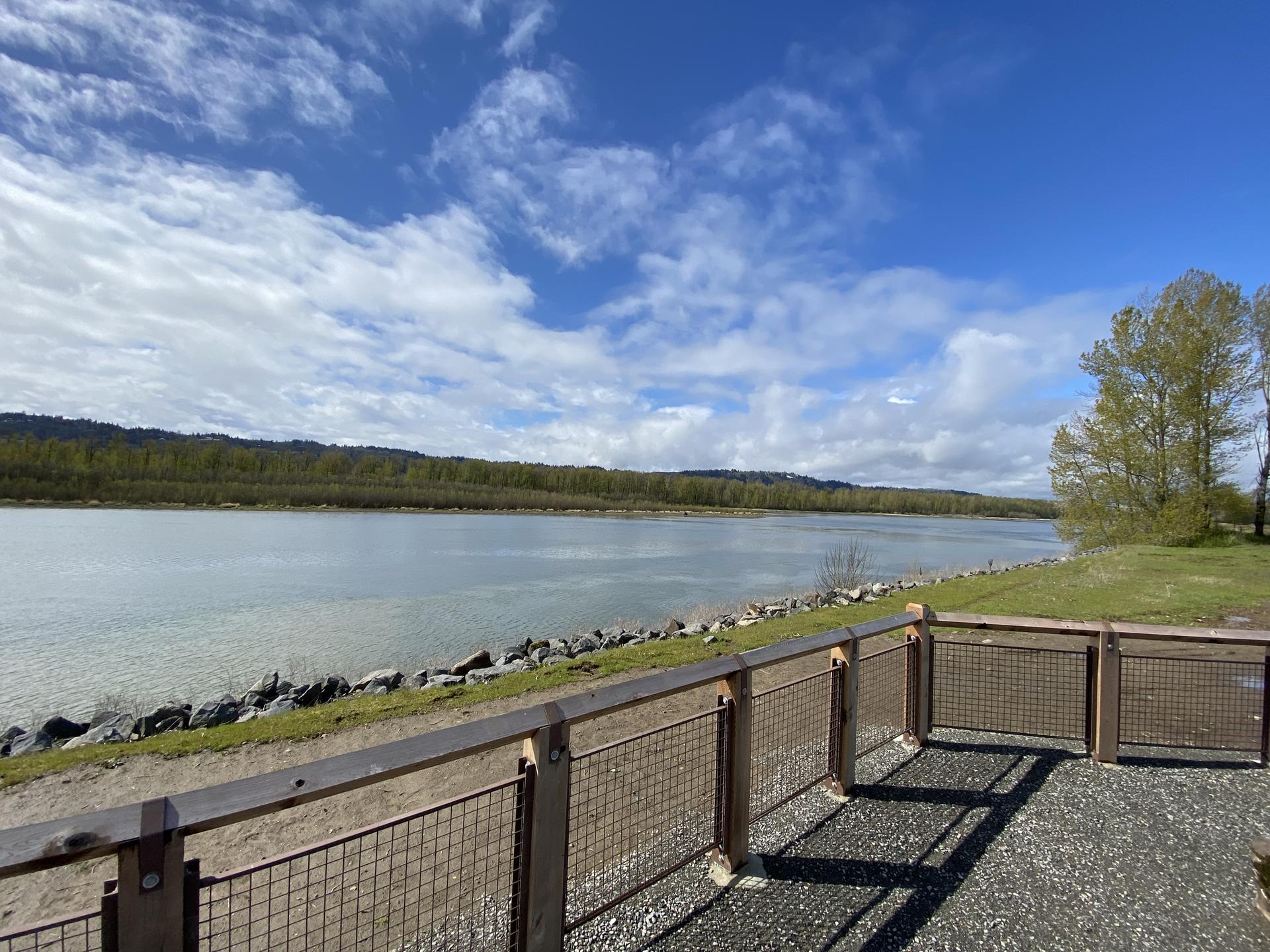Wide river with a forested bank under a partly cloudy sky.