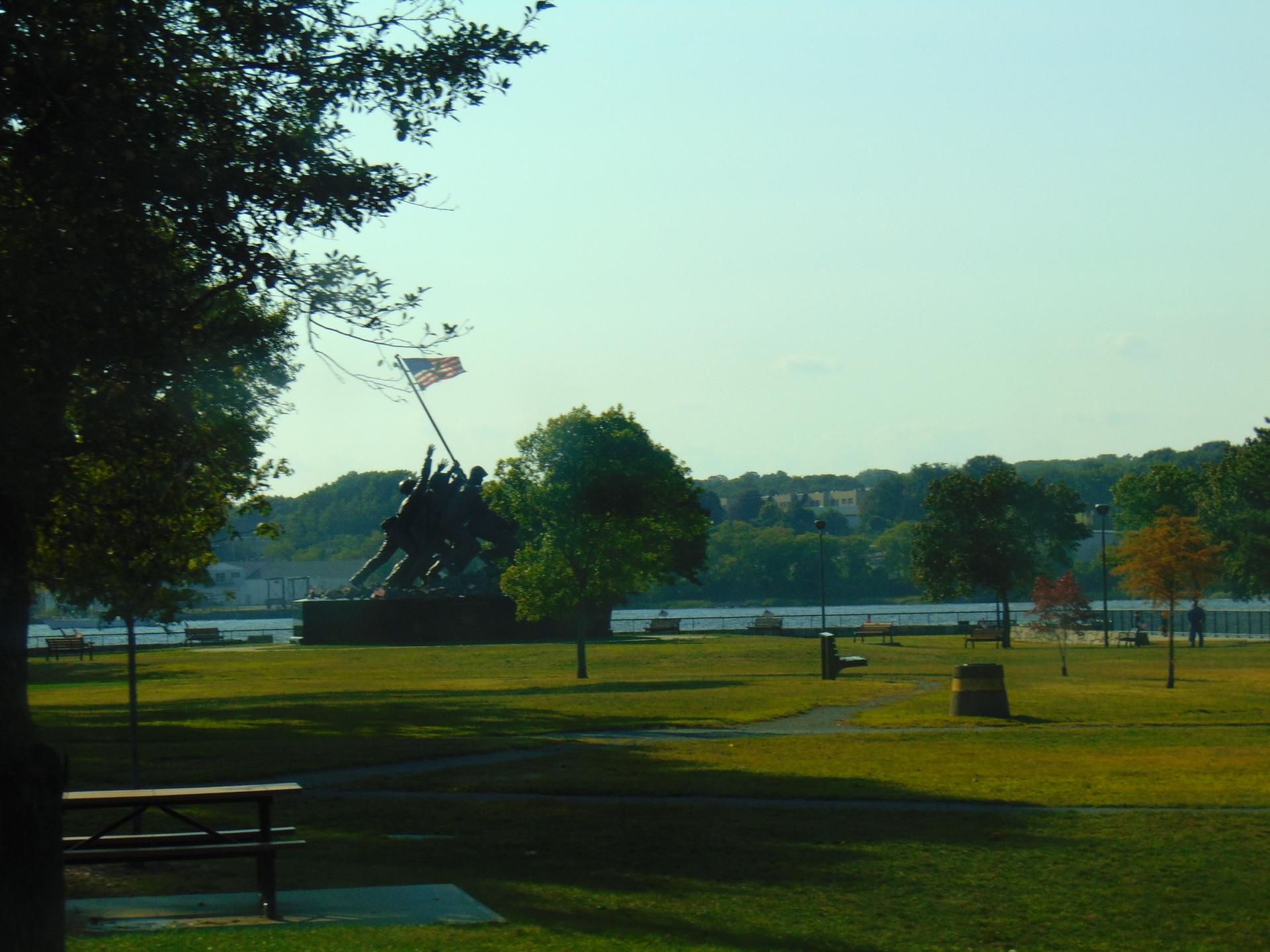 Large statue of figures raising a flag in a sunny park by water.