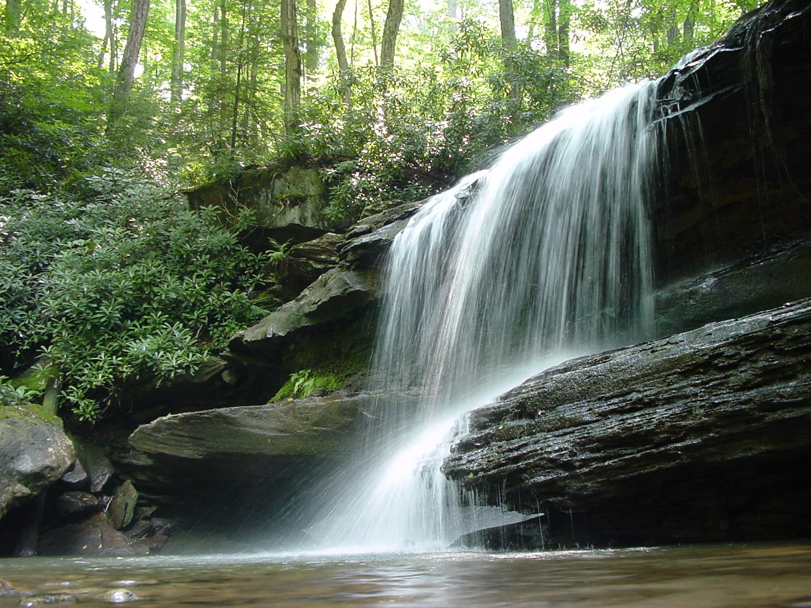 A beautiful waterfall cascades over dark rock formations into a clear pool.