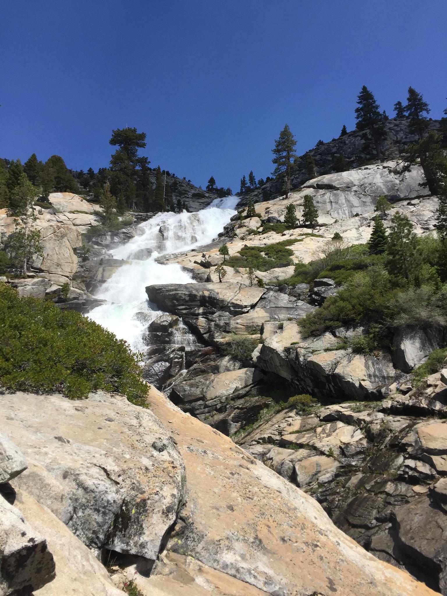 A large waterfall tumbles down a rocky mountain face under a clear sky.