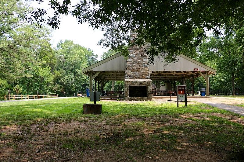 A large picnic shelter with a stone fireplace stands in a grassy clearing.