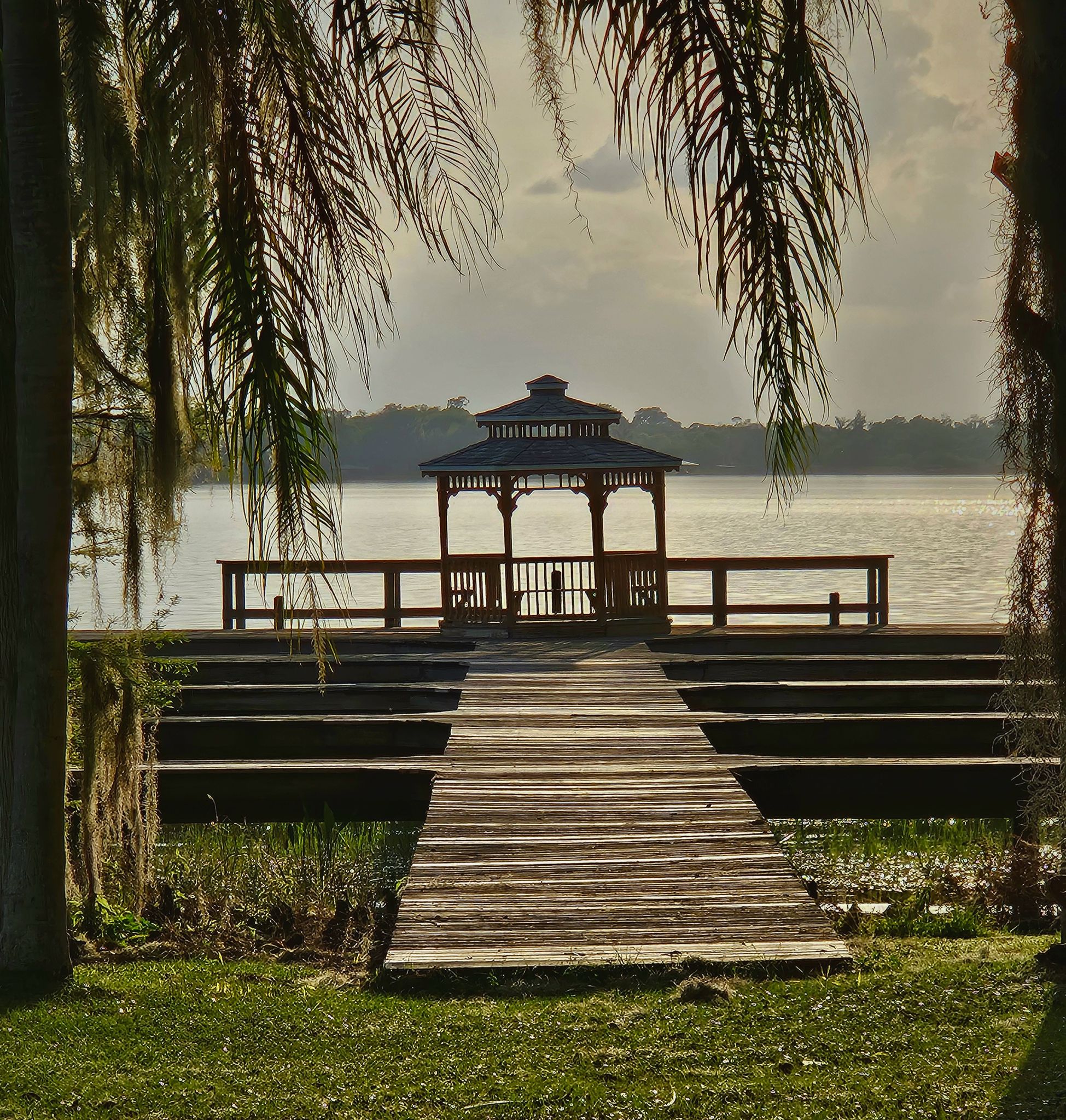 Wooden dock leading to a lakeside gazebo, framed by hanging foliage in soft light. - Lake Marion – Lake Hamilton loop from Winter Haven