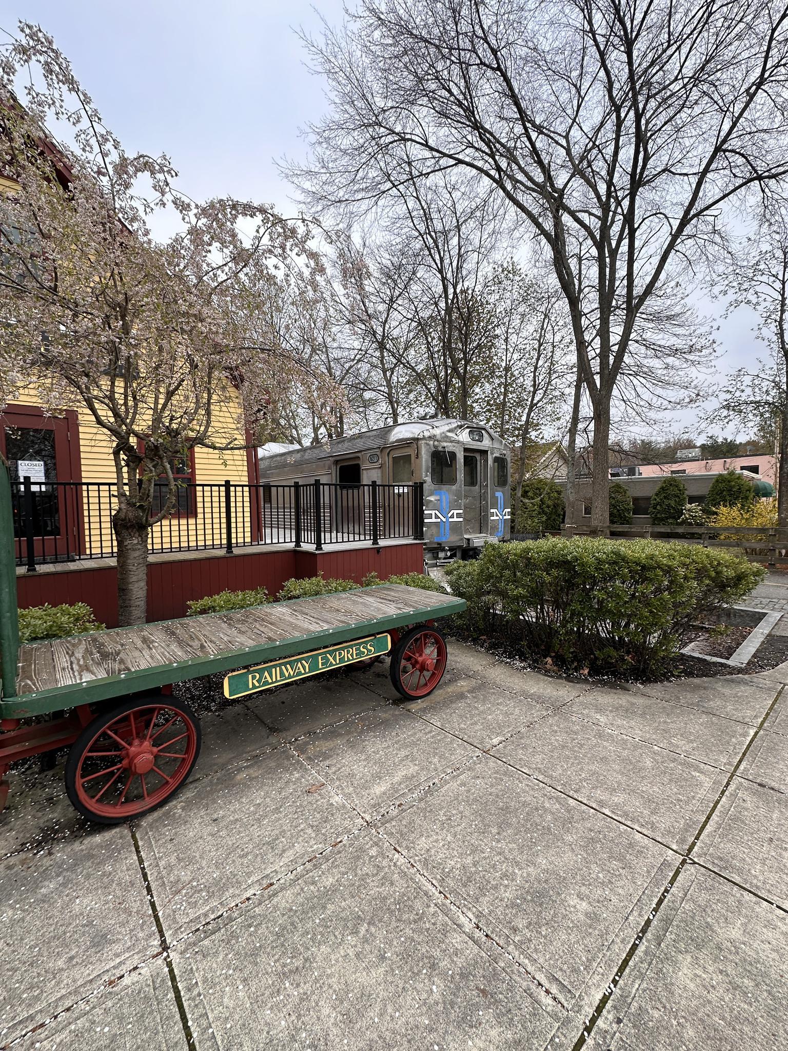 Old railway cart and train car next to a building under bare trees.
