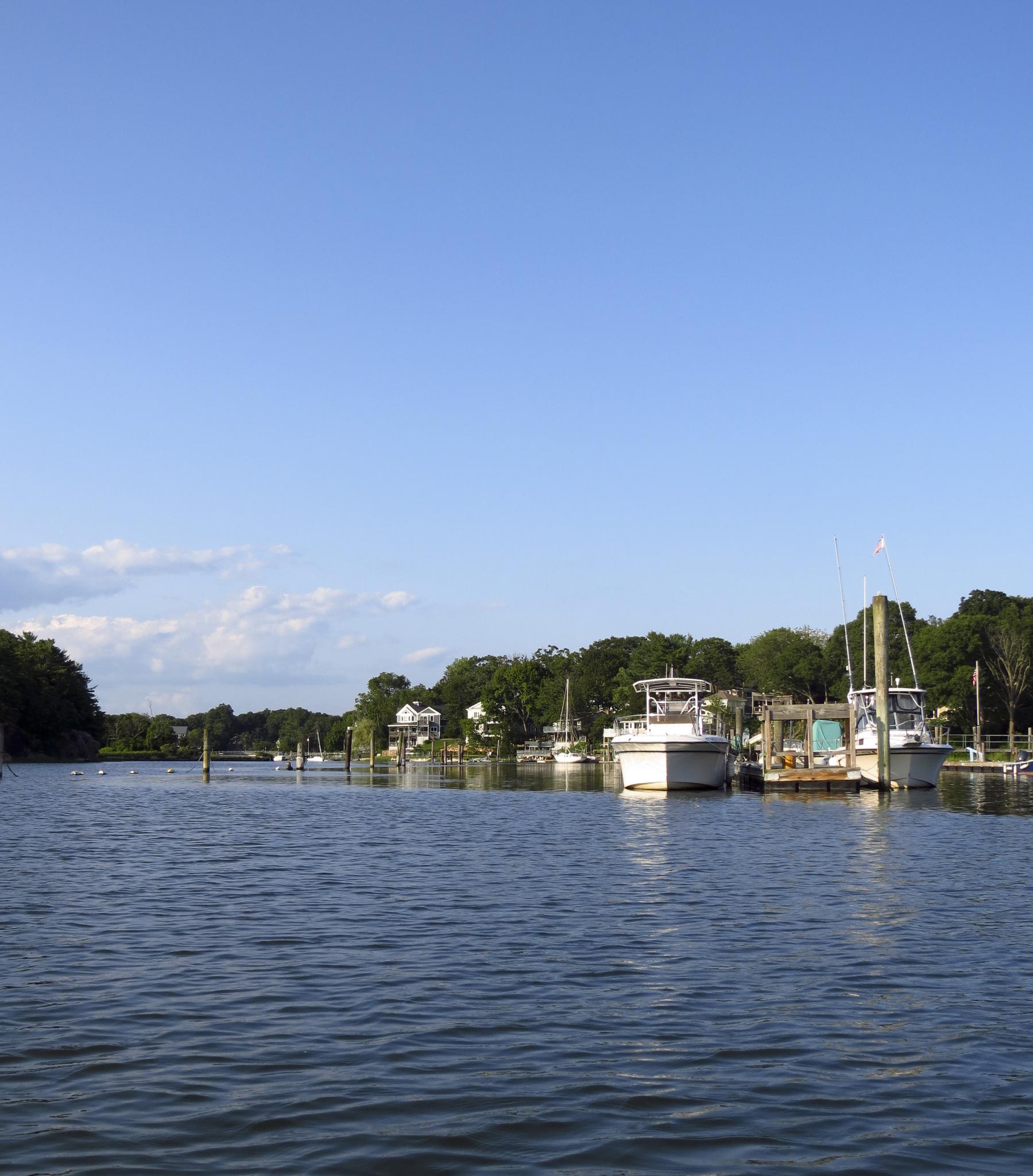 Boats docked along a tree-lined shore under a clear blue sky.