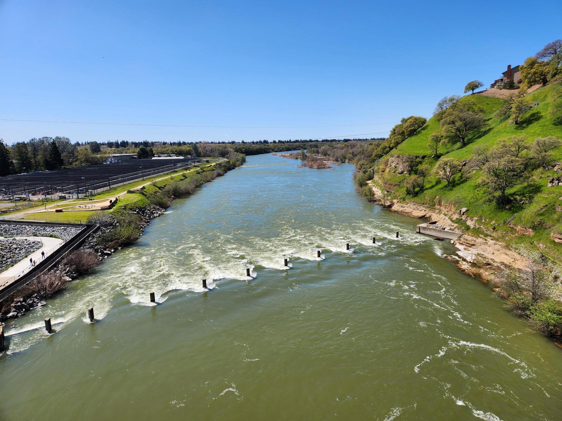 Wide river with rapids and a dam structure under a clear blue sky.