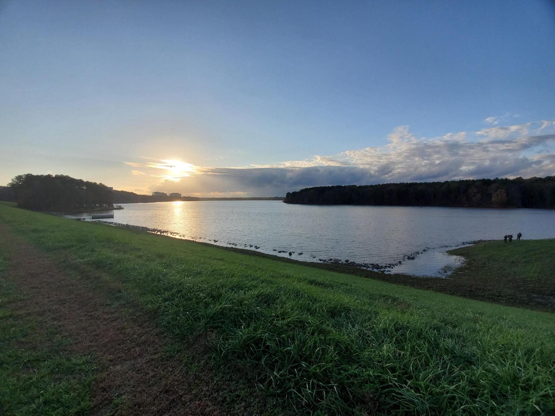 Golden sunset over a wide lake with forested shores and grassy foreground.