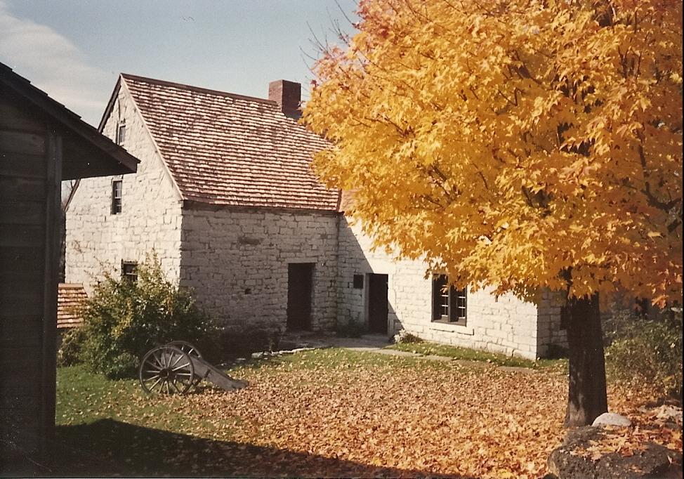 An old stone building with a vibrant yellow autumn tree and cannon.
