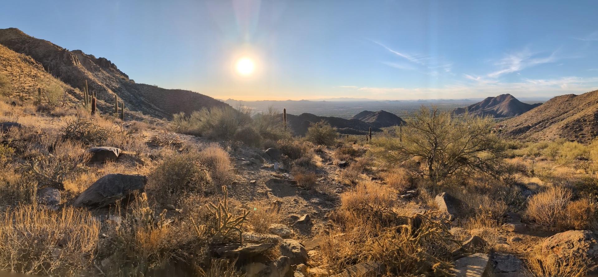 Panoramic desert mountain view with bright sun low in the sky.
