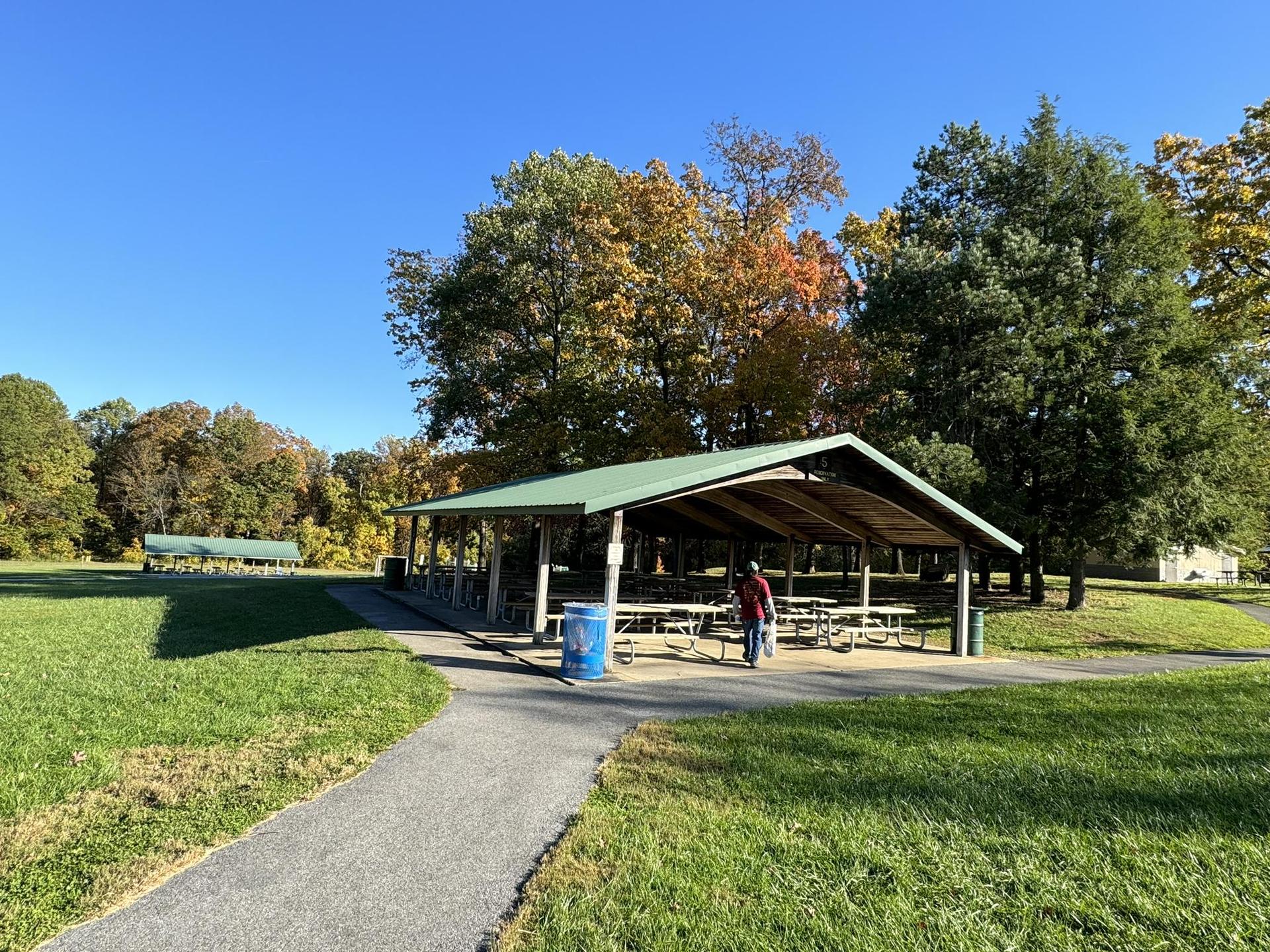 Person walking near a picnic pavilion in a park on a sunny autumn day.