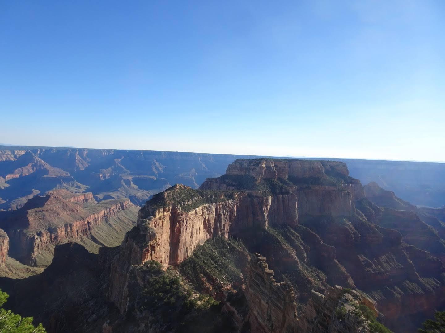 Expansive, sunlit canyon with layered rock formations under a clear blue sky.