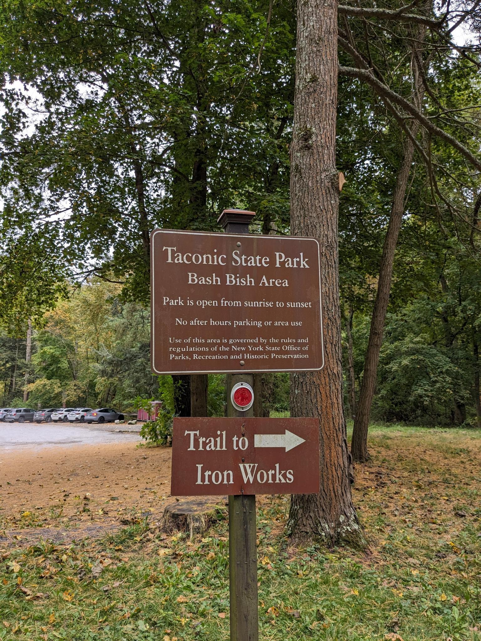 Brown park signs on a pole, pointing to a trail entrance.