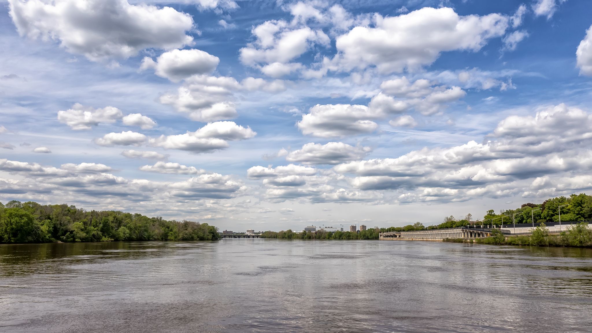 Wide river under a bright, cloudy sky, flanked by green trees. - Crosswicks Creek footbridge – Delaware River loop from Bordentown