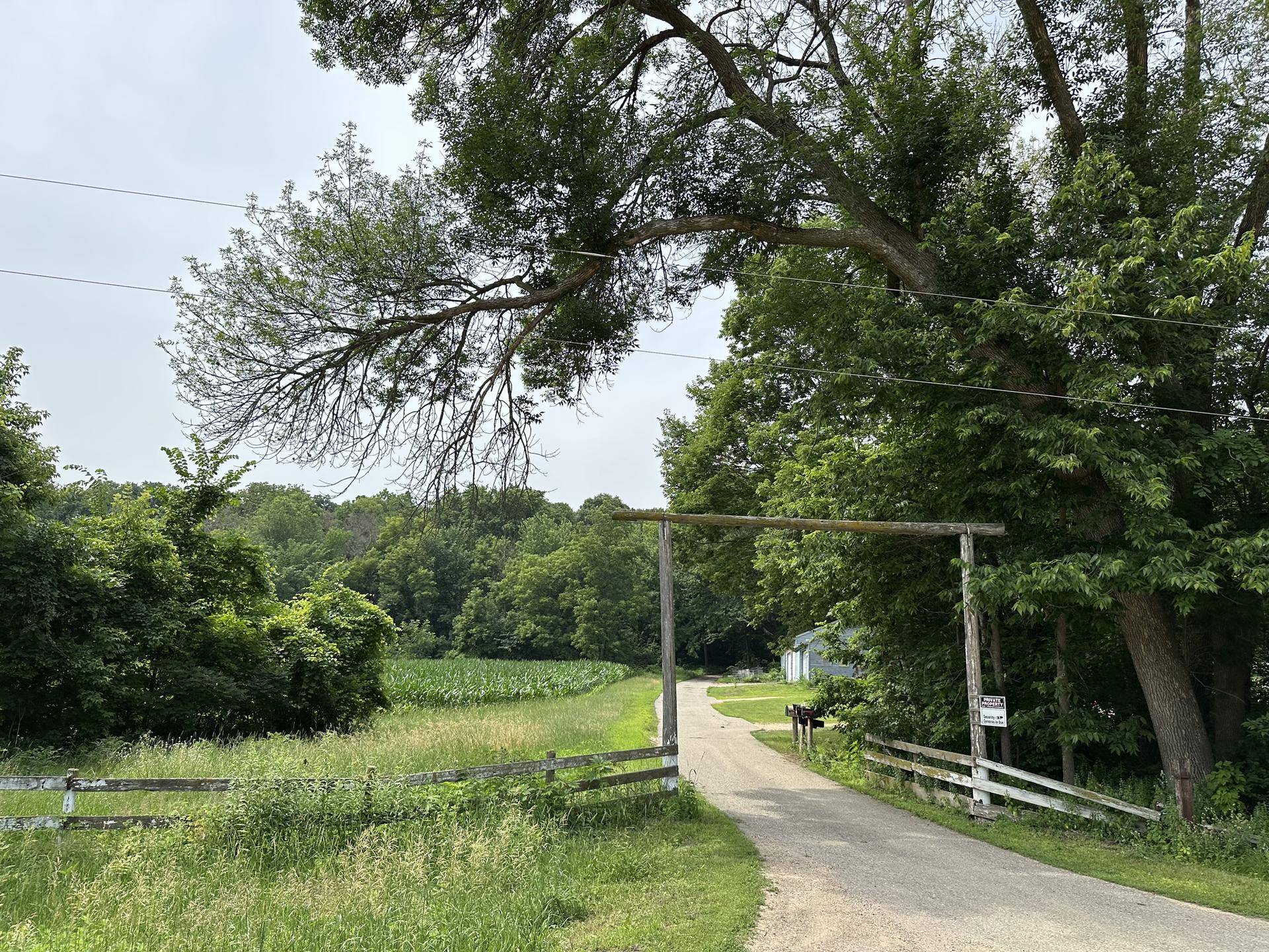 A dirt road passes under a wooden archway into a green forested area.