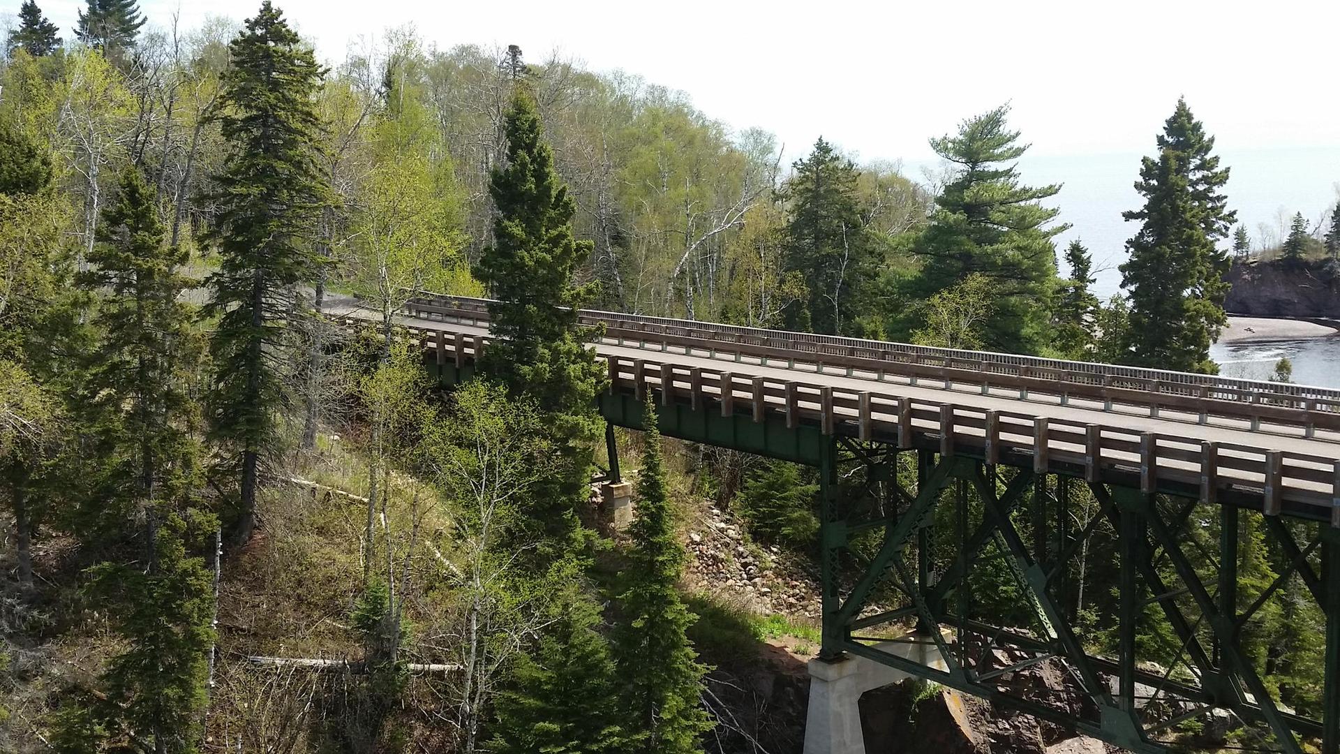 A long green bridge spans a forested valley on a bright day.