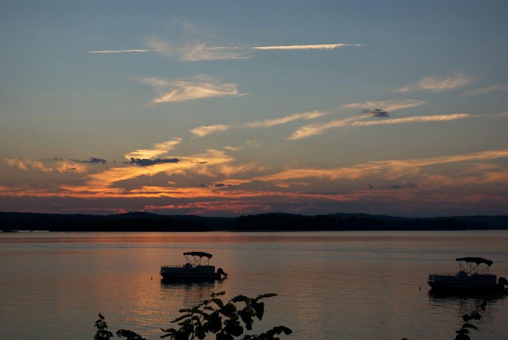 Two boats on calm water at sunset with a colorful sky.