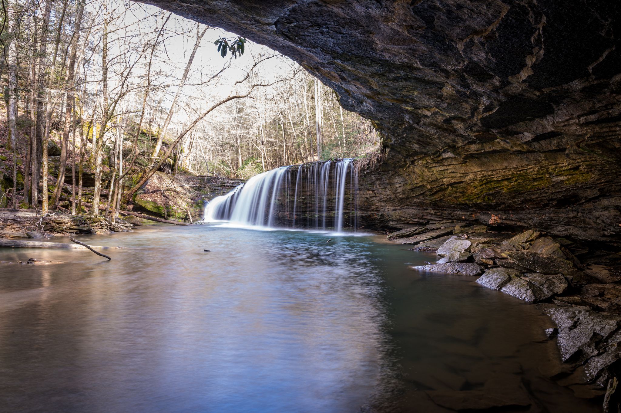 A waterfall cascades into a pool under a large, dark rock overhang. - Lick Creek and Princess Falls Trail