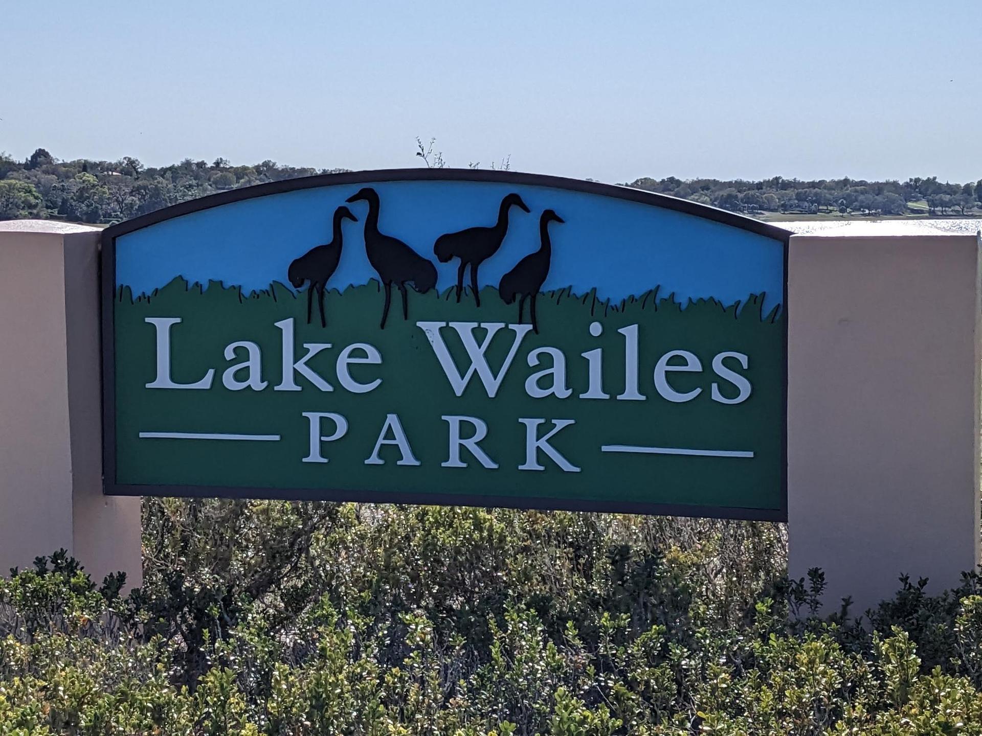 A park sign with bird silhouettes under bright sun, green bushes below.