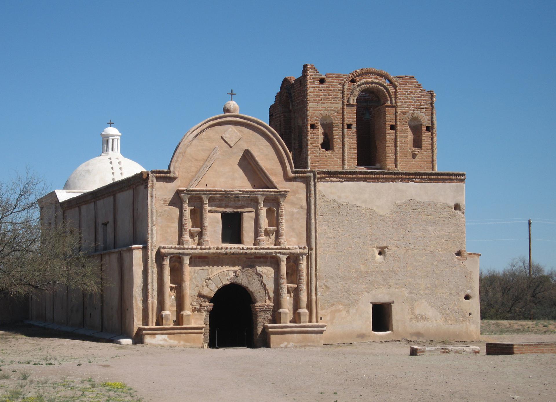 Weathered mission-style building with a dome and crumbling tower under a clear sky.