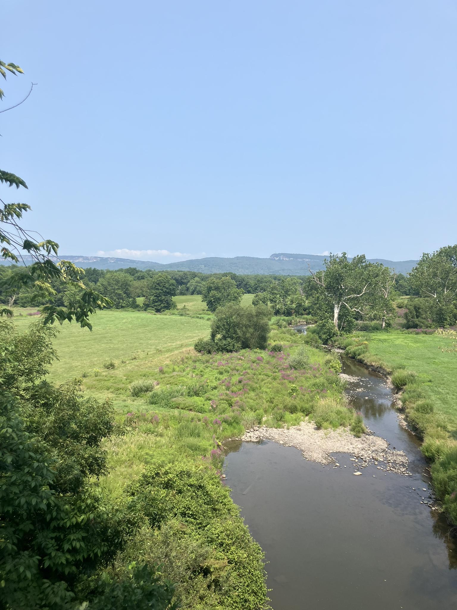 Sunny aerial view of a winding river through vast green fields and mountains.