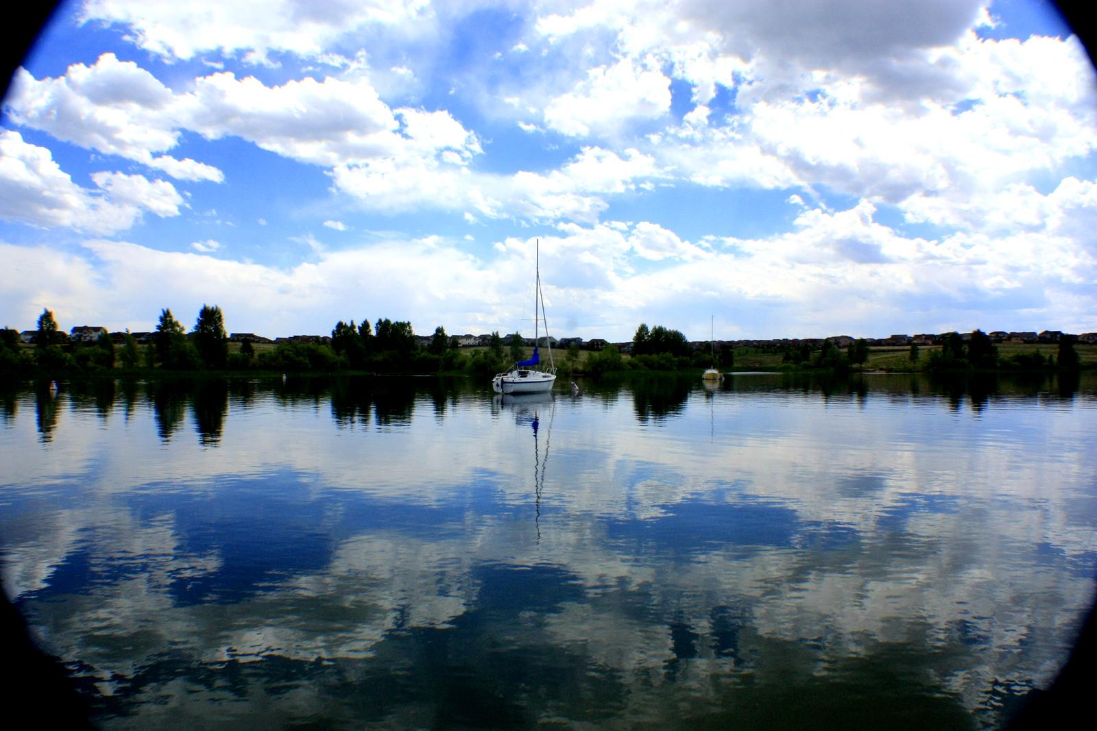 Sailboat on a calm lake under a bright, cloudy sky with reflections.