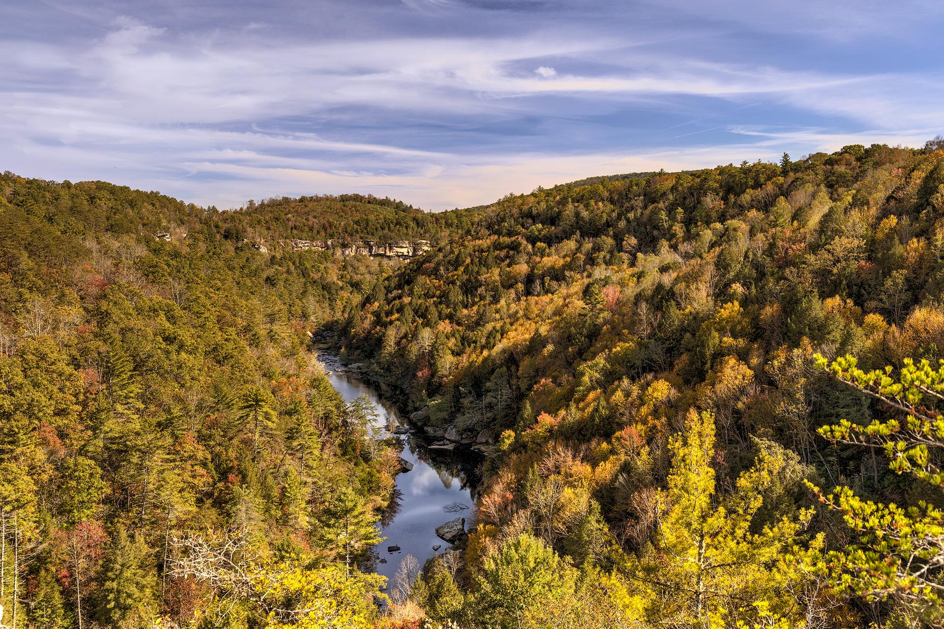 A river winds through a valley of colorful autumn trees under a blue sky.
