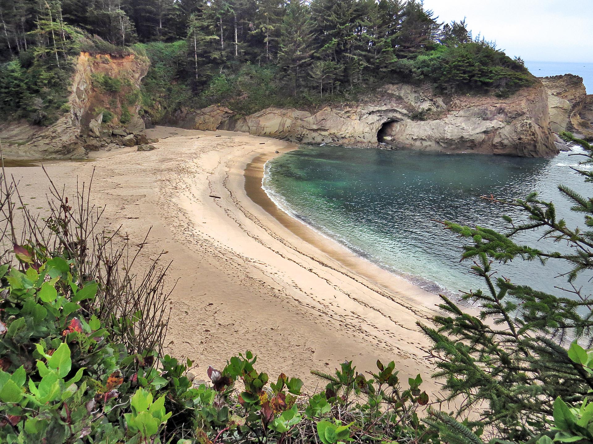 Secluded sandy beach cove with clear water, rocky cliffs, and a sea cave.