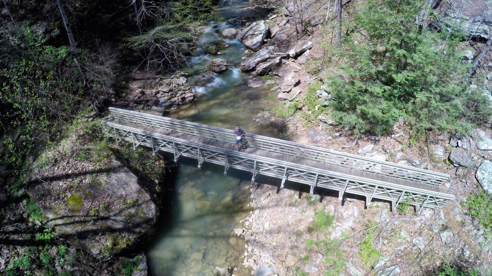 Aerial view of a person walking on a wooden bridge over a rocky stream.
