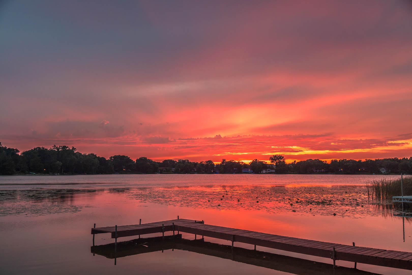 Vibrant red and orange sunset over a lake with a wooden dock.