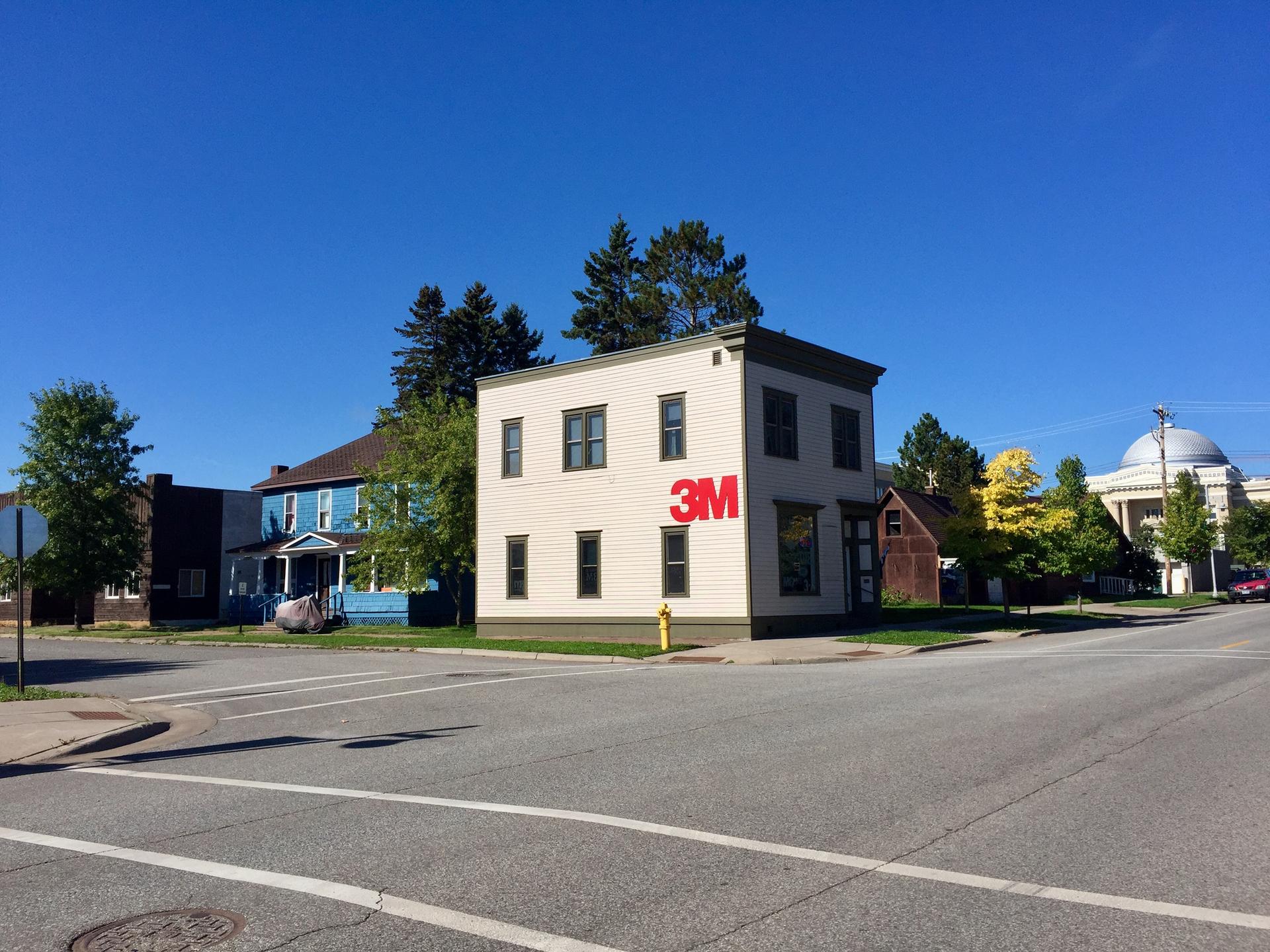 A small commercial building with a '3M' logo under a clear blue sky.
