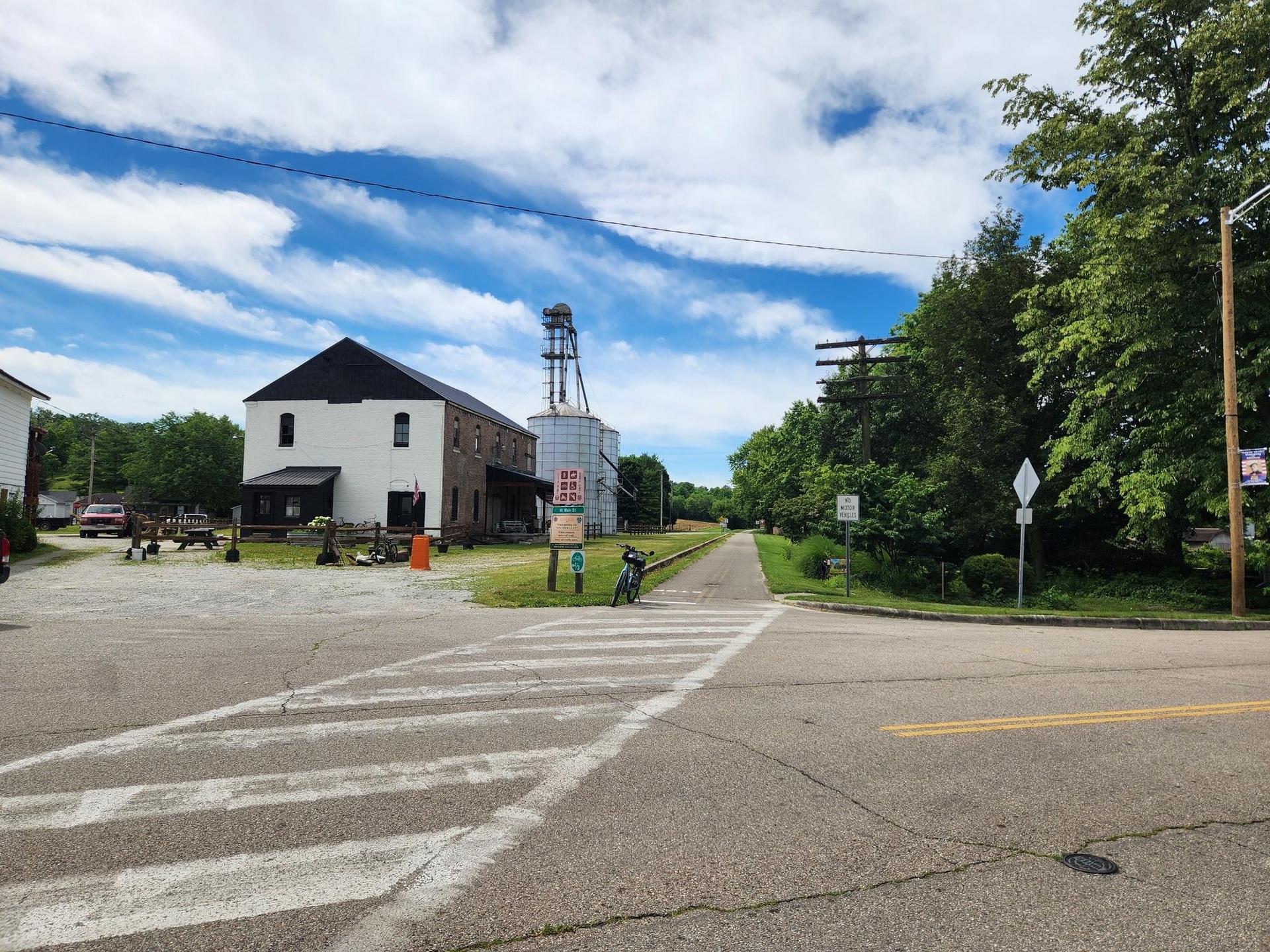 Road intersection with a building, grain silos, and a parked bicycle.