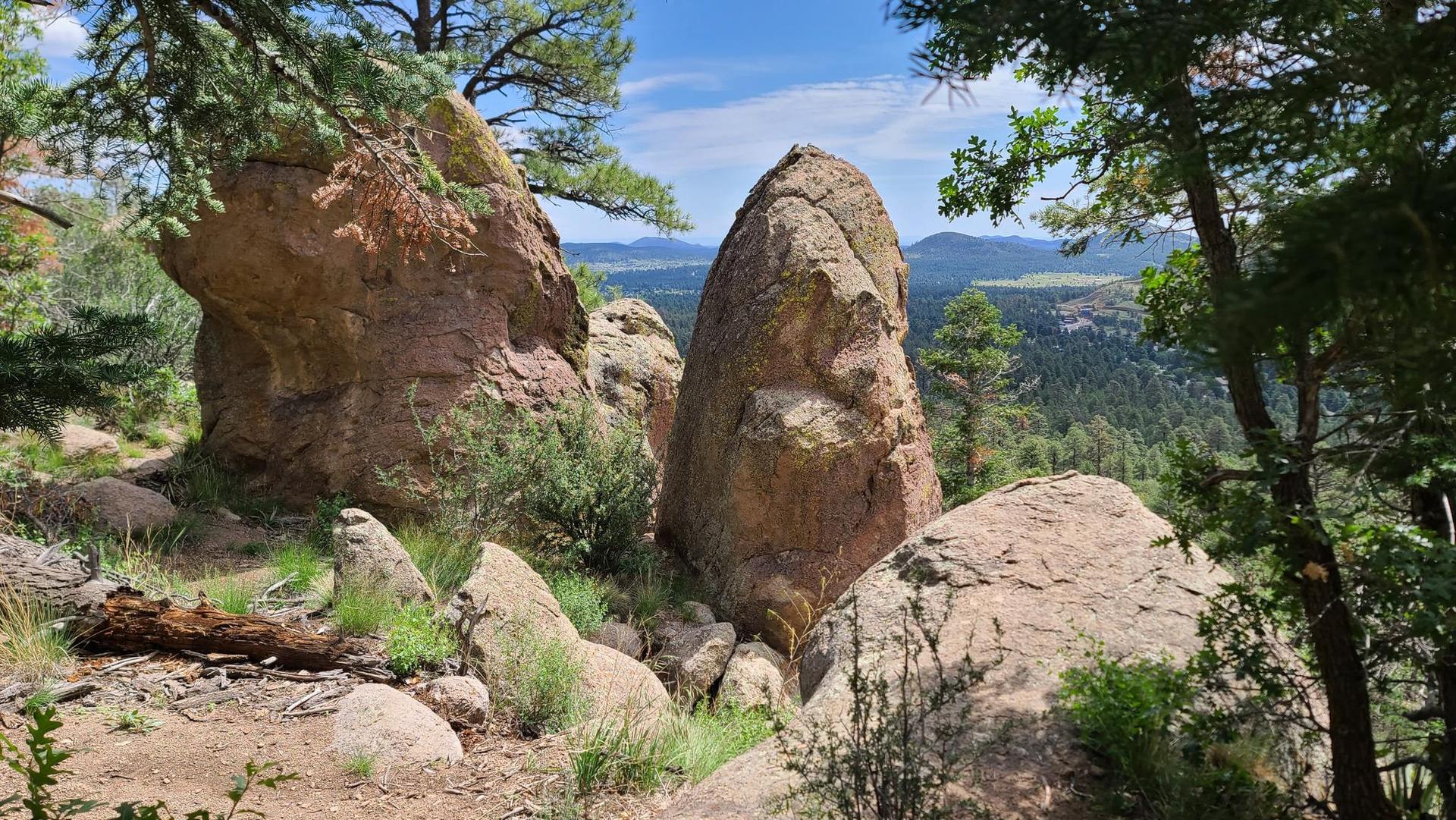 Large rock formations on a hillside with distant mountains and green trees.