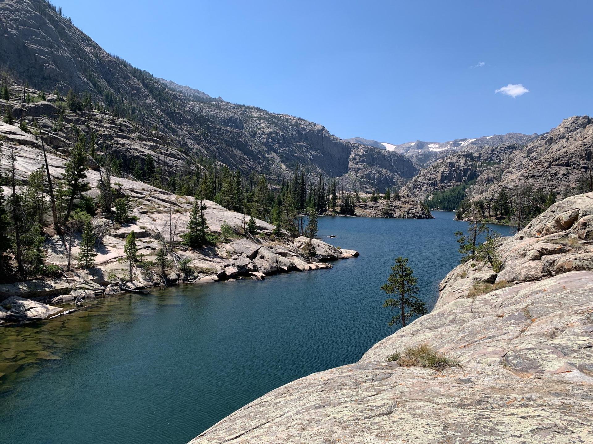 A clear blue mountain lake surrounded by rocky, forested slopes on a sunny day.