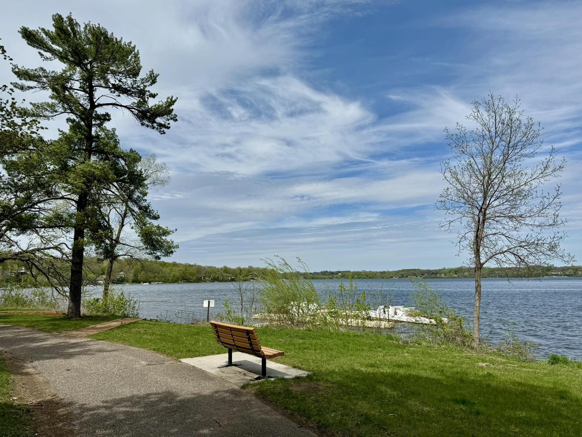 Empty park bench on a paved path overlooking a wide lake.