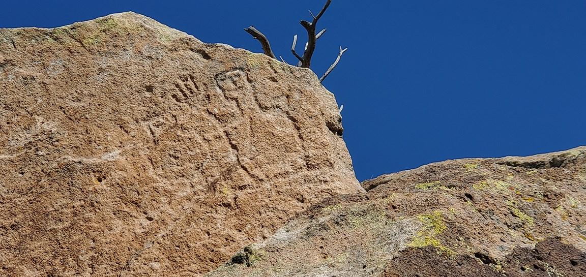Ancient carvings on a sunlit rock face against a clear blue sky.