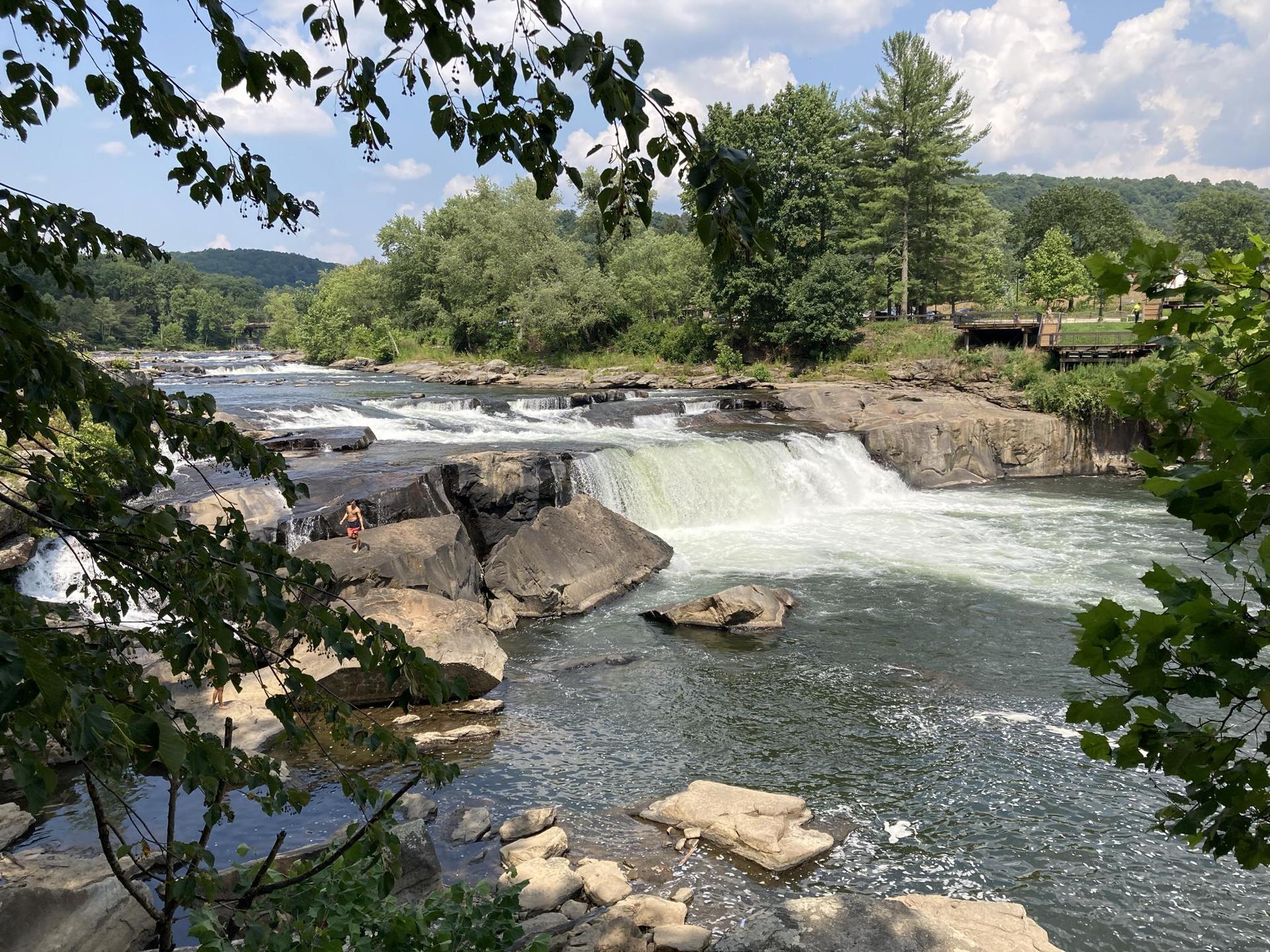 Daylight view of a wide waterfall cascading over rocks into a river.