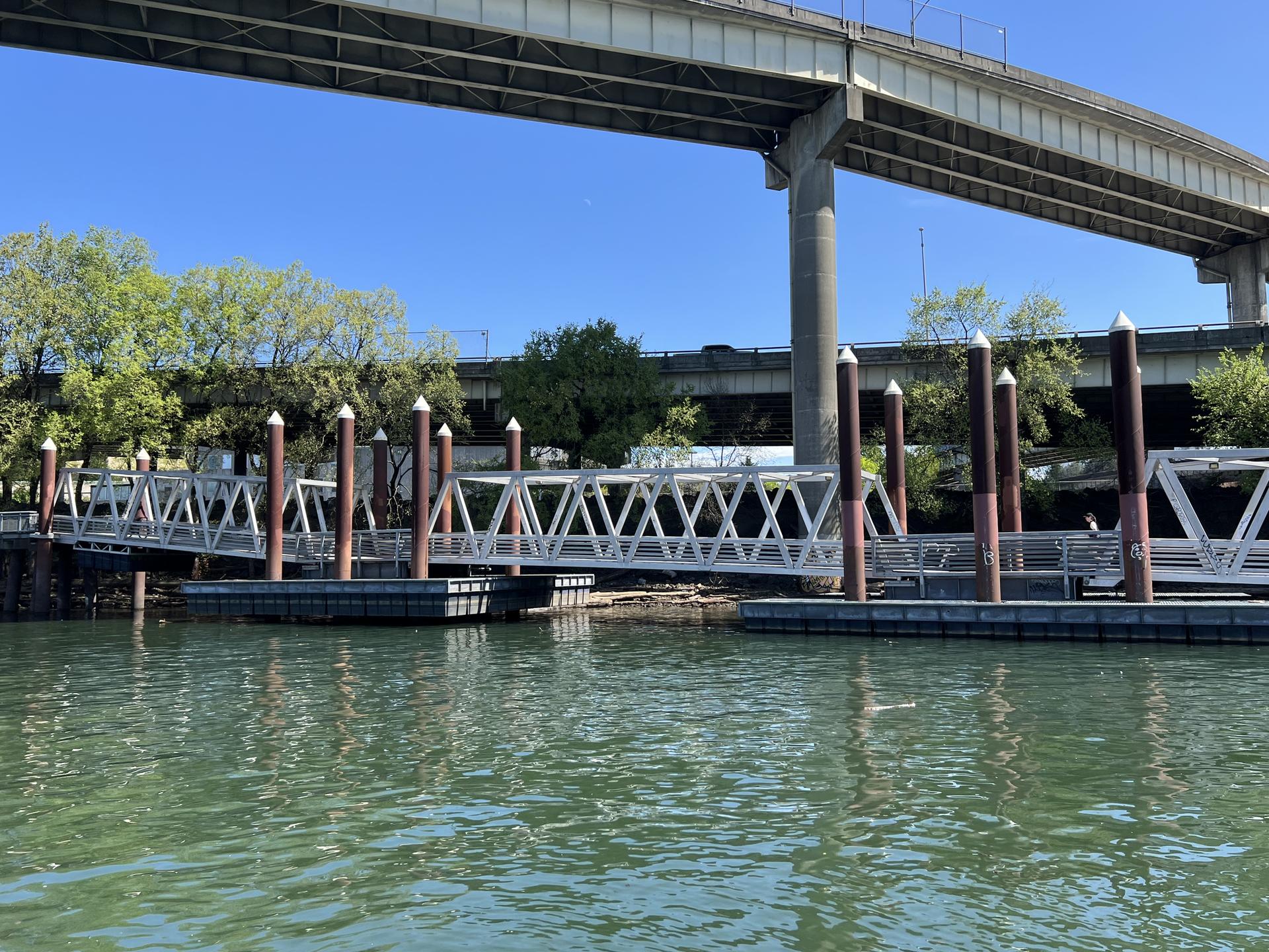 Floating docks and a large concrete bridge over a river on a sunny day.