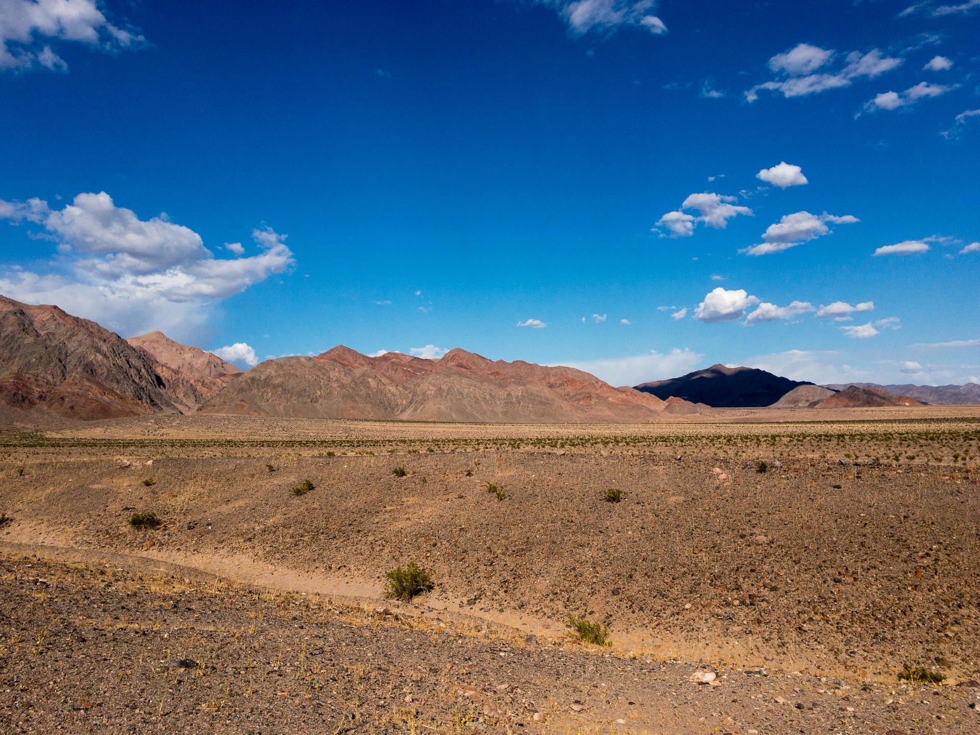 Expansive desert landscape with rocky mountains under a bright blue sky.