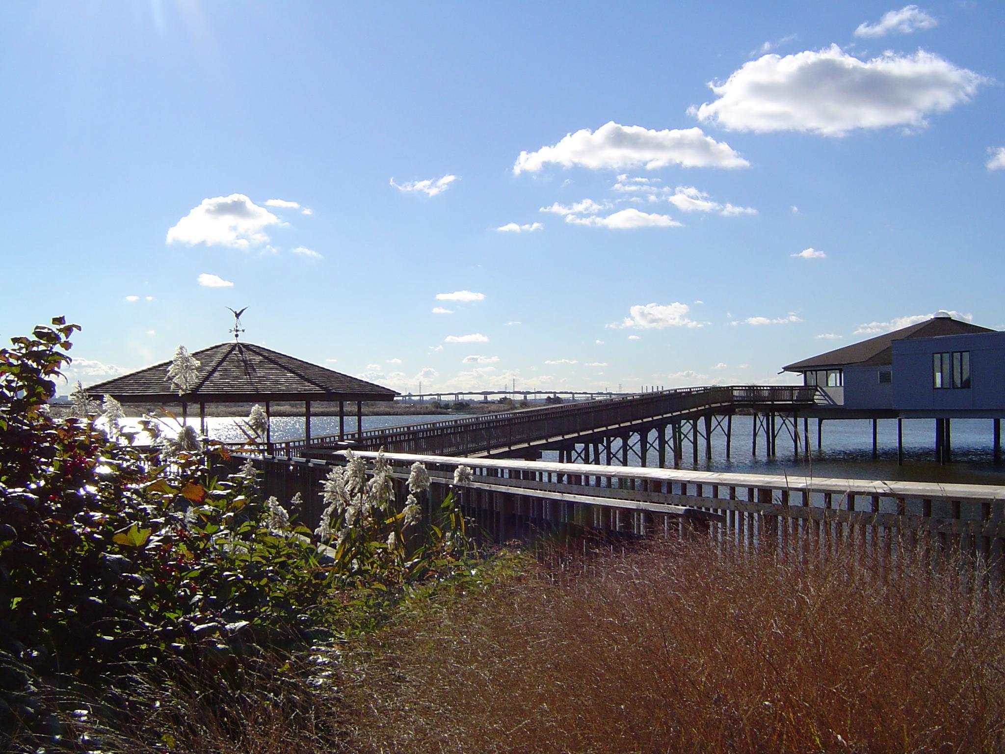 Long wooden boardwalk and buildings extend over water on a sunny day.