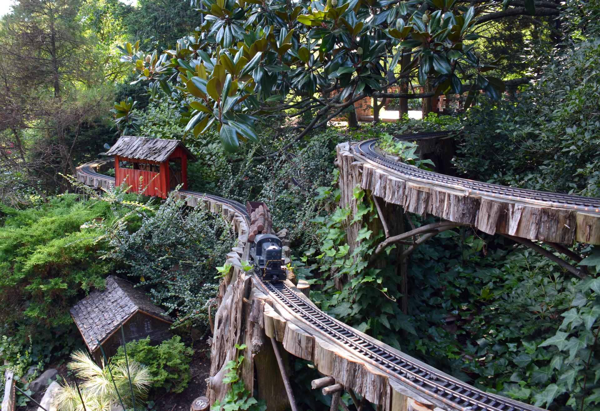 Miniature train on elevated wooden tracks winding through a lush green garden.