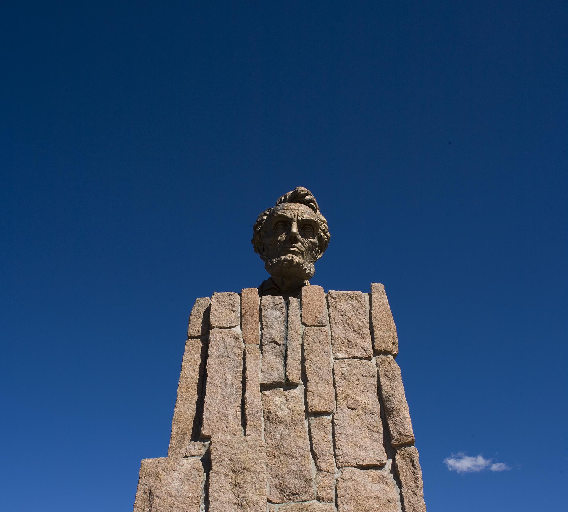 Stone bust of a man on a pedestal against a clear blue sky.