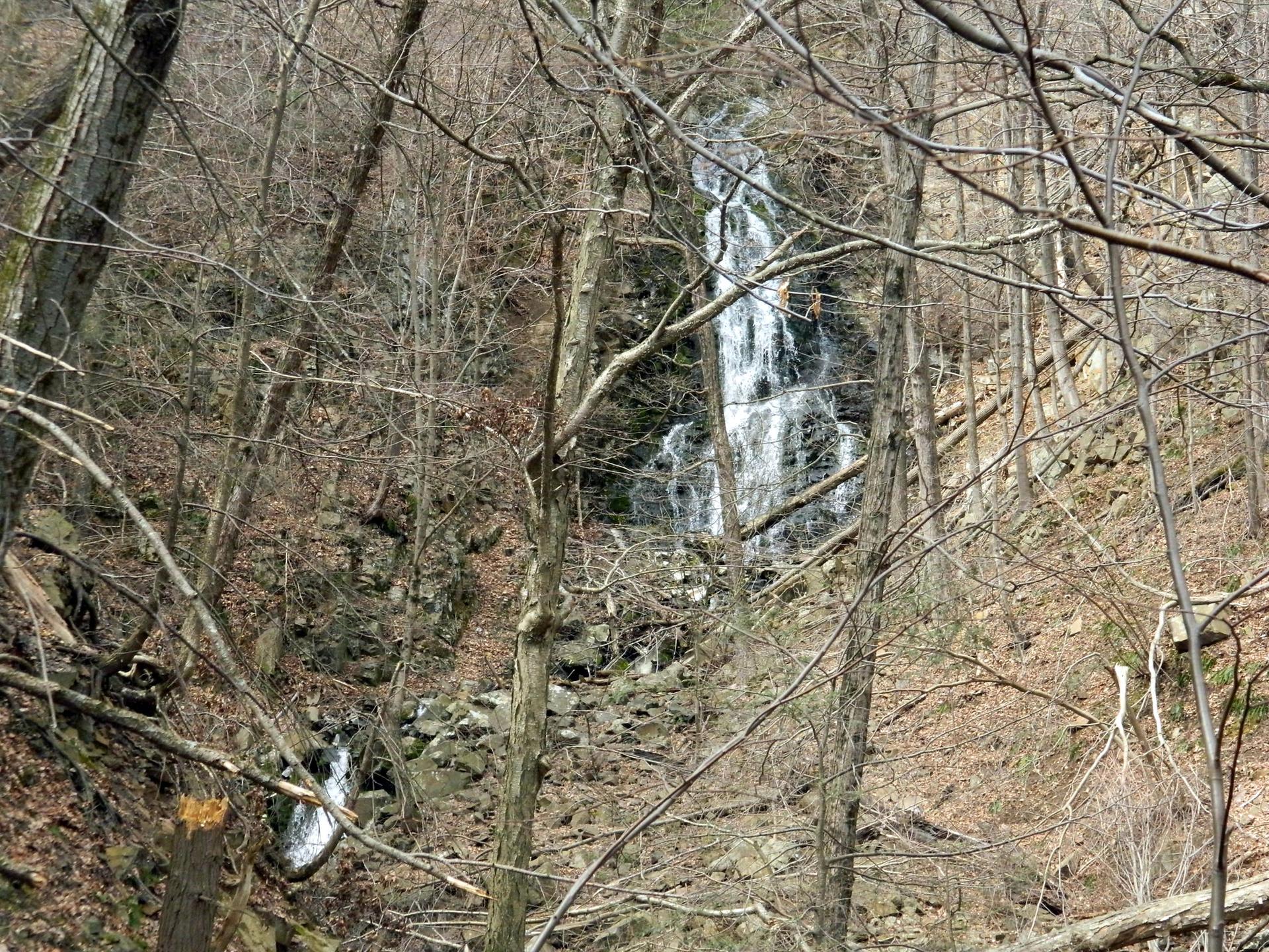 A tall waterfall cascades through a bare winter forest with rocks.