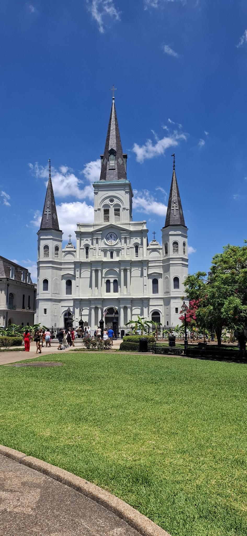 A majestic cathedral with spires overlooks a vibrant green lawn on a sunny day.