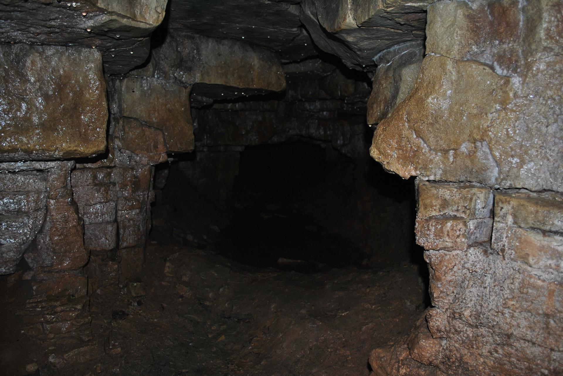 Dark, narrow cave passage with rough rock walls and floor.