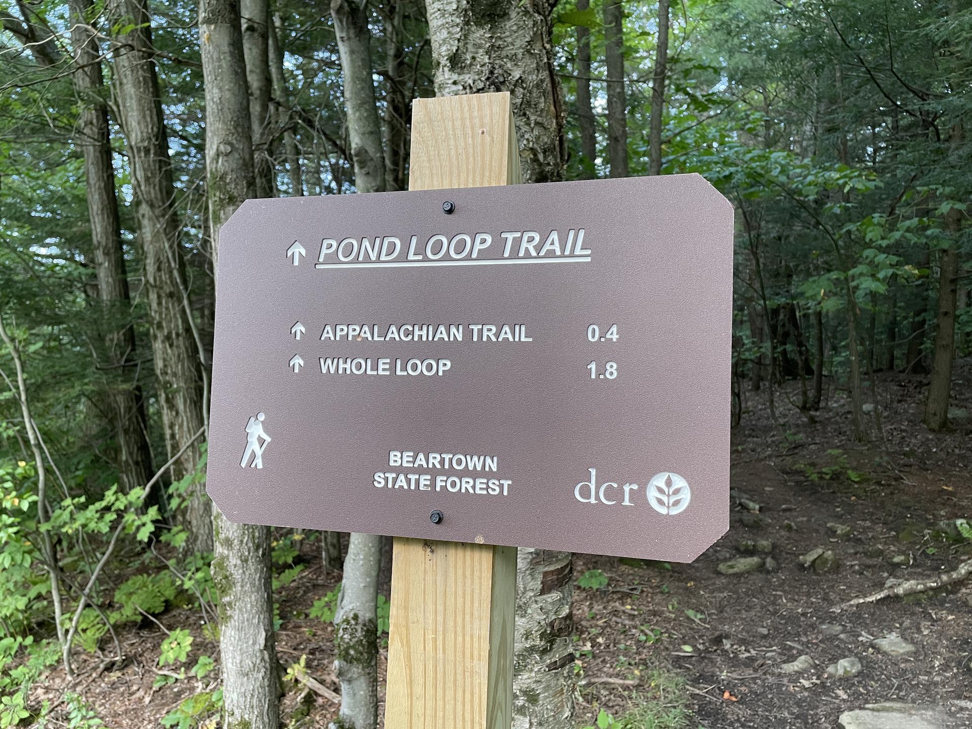 A brown trail sign on a wooden post, surrounded by green trees.