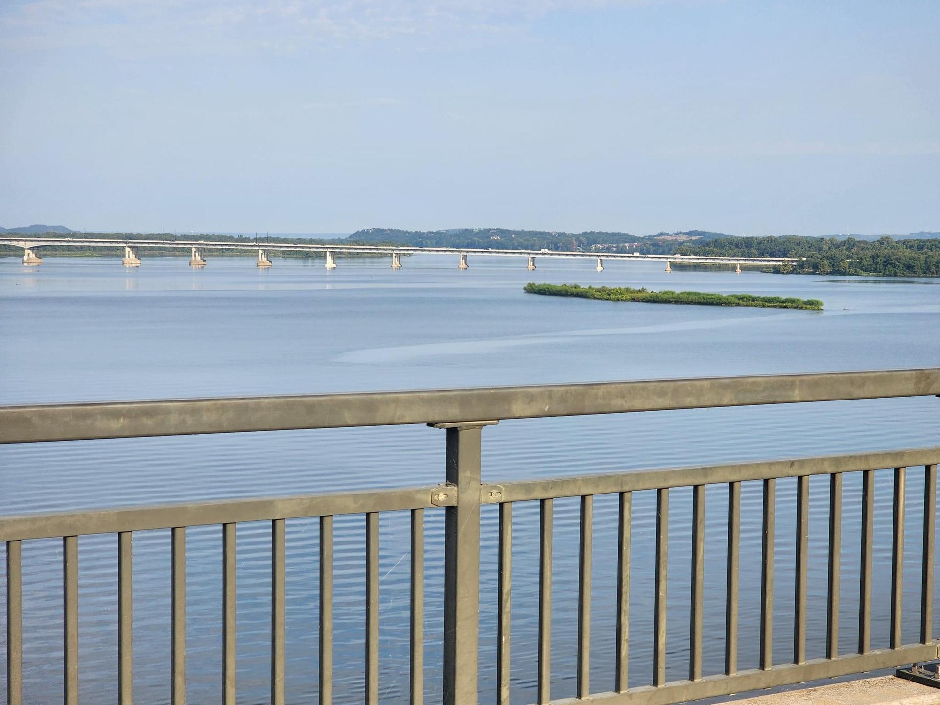 View of a wide river with a distant bridge from behind a railing.