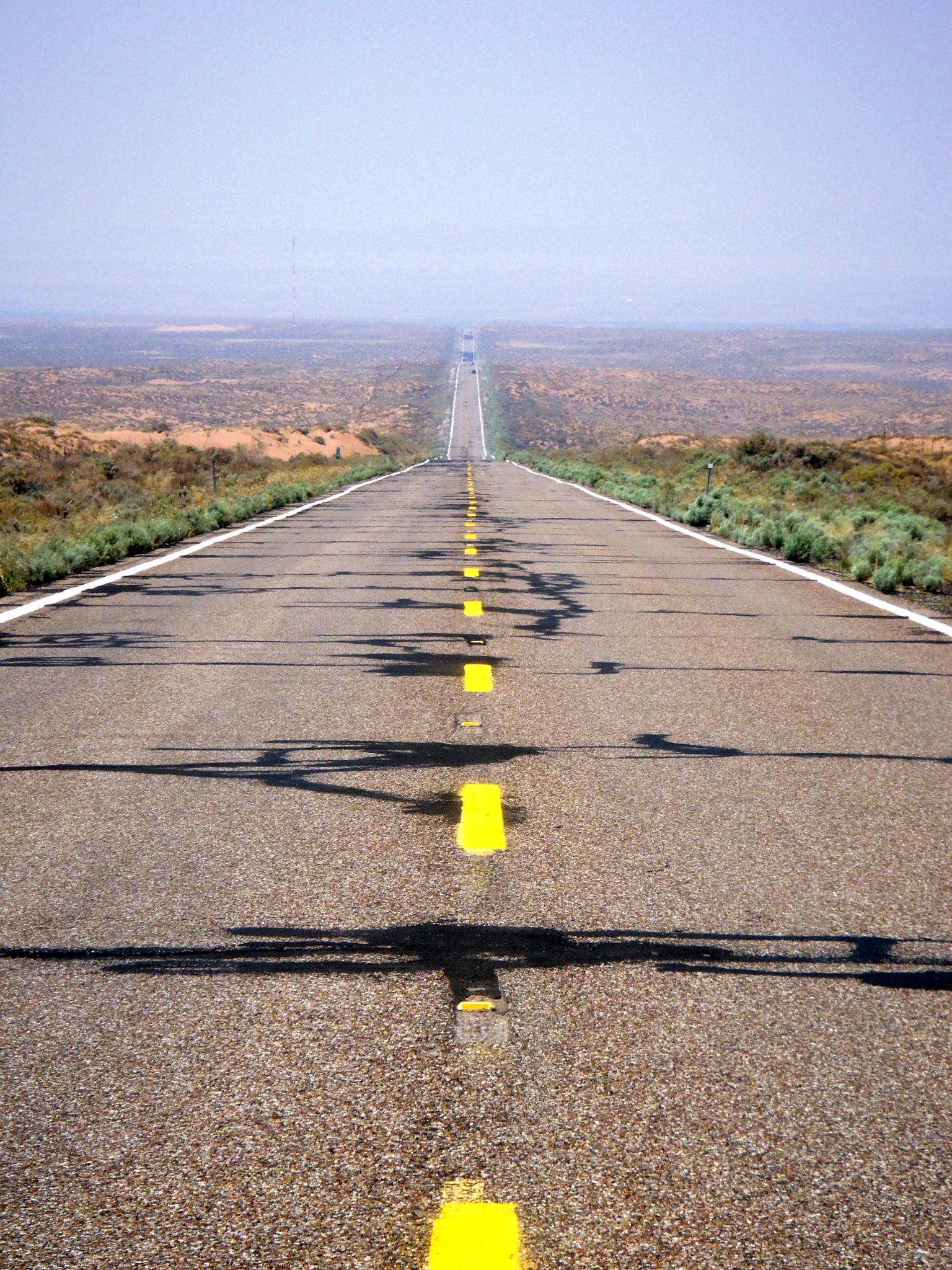 Long, straight desert road with yellow markings stretching into the distance.